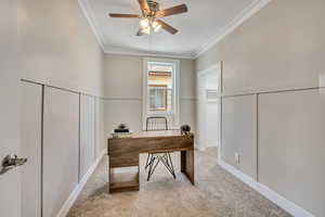 Bedroom/home office featuring a ceiling fan, light colored carpet, crown molding, decorative wall and walk in closet