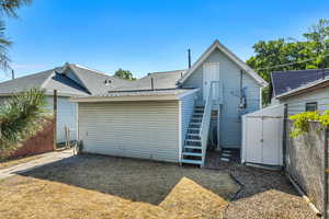 Rear view of property with a shingled roof, a storage shed, attic access and stairs