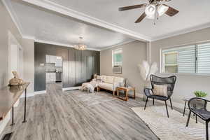 Living area with a textured ceiling, accent wall, light wood-type flooring, crown molding, ceiling fan, and cooling unit