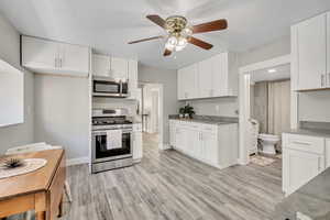 Kitchen featuring appliances with stainless steel finishes, ceiling fan, white cabinets, light countertops, and light wood-style flooring