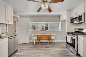 Kitchen featuring stainless steel appliances, ceiling fan, light wood-style flooring, white cabinets, and light countertops