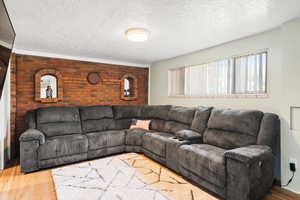 Living area with brick wall, wood finished floors, a textured ceiling, and an accent wall