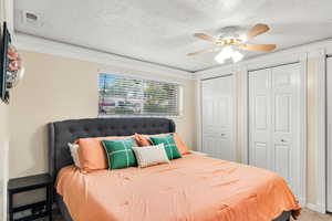 Bedroom featuring two closets, crown molding, a textured ceiling, a ceiling fan, and carpet