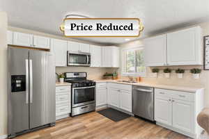 Kitchen with stainless steel appliances, a textured ceiling, white cabinets, light countertops, and light wood finished floors