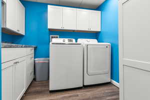 Laundry room with washing machine and clothes dryer, cabinet space, and wood finished floors