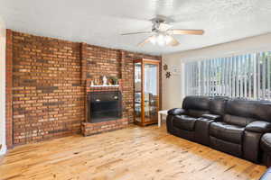 Living area with wood finished floors (this area is getting carpet), a textured ceiling, ceiling fan, a fireplace, and brick wall