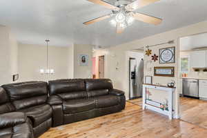 Living room with light wood-style flooring(this area is getting carpet), a textured ceiling, a ceiling fan, and a chandelier
