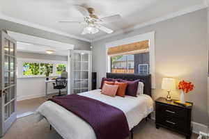 Carpeted bedroom with french doors, multiple windows, ornamental molding, and a ceiling fan