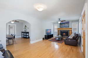 Living area with ceiling fan, arched walkways, light wood-type flooring, and a tiled fireplace