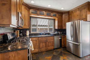 Kitchen with stainless steel appliances, brown cabinets, tasteful backsplash, dark countertops, and dark stone finish floors