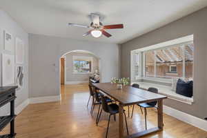 Dining area with arched walkways, light wood finished floors, and a ceiling fan