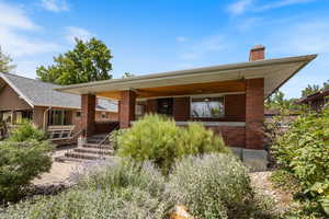 Back of house featuring a chimney, brick siding, and covered porch
