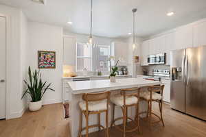 Kitchen featuring stainless steel appliances, a kitchen breakfast bar, tasteful backsplash, light countertops, and recessed lighting