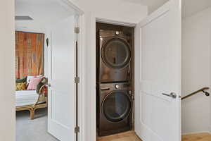 Washroom featuring stacked washing machine and dryer and light colored carpet