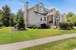 View of front of home with a chimney, a front yard, brick siding, and stucco siding