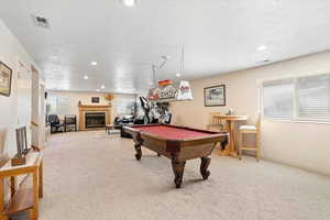 Rec room featuring a textured ceiling, carpet floors, plenty of natural light, pool table, and a glass covered fireplace