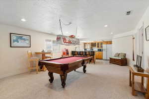 Game room featuring light carpet, bar with sink, a textured ceiling, pool table, and recessed lighting