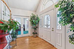 Foyer entrance featuring french doors, light wood finished floors, and high vaulted ceiling