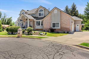 View of front of house featuring concrete driveway, brick siding, a garage, stucco siding, and a front lawn