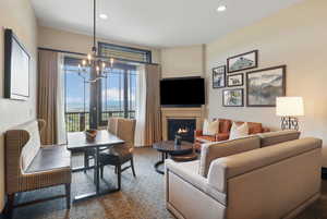Living area with a chandelier, a warm lit fireplace, dark colored carpet, and recessed lighting