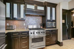 Kitchen with stainless steel appliances, tasteful backsplash, light stone counters, and glass insert cabinets