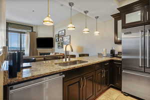 Kitchen with stainless steel appliances, light stone counters, glass insert cabinets, and dark brown cabinetry