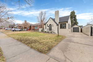 View of front facade with concrete driveway, a detached garage, an outbuilding, and a chimney