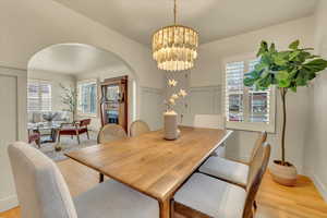Dining space with arched walkways, light wood finished floors, healthy amount of natural light, a chandelier, and a decorative wall