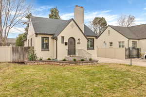 View of front of home with a chimney, roof with shingles, brick siding, and a patio