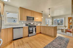 Kitchen with appliances with stainless steel finishes, light brown cabinets, light wood-style flooring, and decorative backsplash