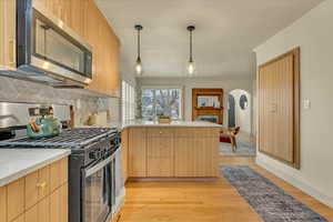 Kitchen with gas range, stainless steel microwave, a peninsula, backsplash, and light wood finished floors