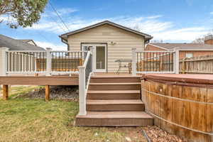 Back of property with a hot tub, a deck, a yard, and stairs