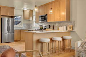 Kitchen featuring stainless steel appliances, a peninsula, light wood finished floors, backsplash, and light countertops