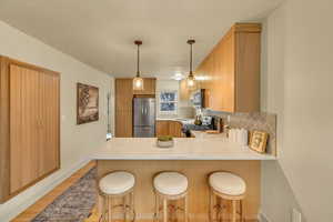 Kitchen featuring stainless steel appliances, a peninsula, backsplash, light wood-style flooring, and light countertops