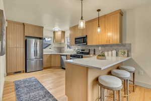 Kitchen with stainless steel appliances, a peninsula, a kitchen breakfast bar, pendant lighting, and tasteful backsplash