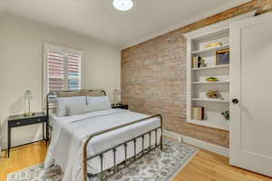 Bedroom featuring brick wall, crown molding, and wood finished floors
