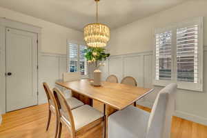 Dining space featuring a chandelier, a decorative wall, a wainscoted wall, and light wood-type flooring