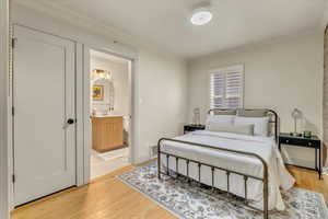 Bedroom with ornamental molding, light wood-type flooring, and ensuite bathroom