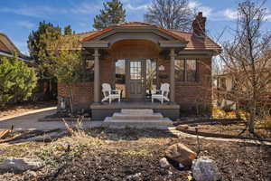 View of front of property with brick siding, a porch, a tile roof, and a chimney