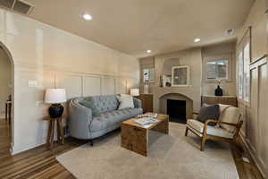 Living area with a decorative wall, arched walkways, wood finished floors, recessed lighting, and a wainscoted wall