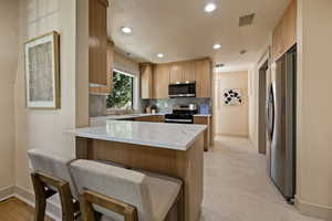 Kitchen with appliances with stainless steel finishes, a peninsula, tasteful backsplash, light stone countertops, and a breakfast bar