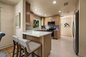 Kitchen featuring stainless steel appliances, a peninsula, backsplash, a breakfast bar area, and recessed lighting