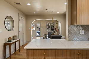 Kitchen featuring arched walkways, a chandelier, backsplash, brown cabinetry, and recessed lighting