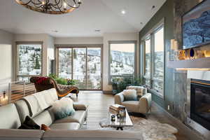 Living area with lofted ceiling, a glass covered fireplace, plenty of natural light, a chandelier, and wood finished floors