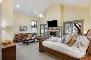Living area featuring high vaulted ceiling, carpet flooring, a chandelier, plenty of natural light, and a glass covered fireplace