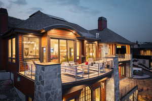Back of house featuring a chimney, a balcony, and a shingled roof