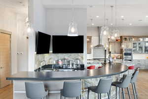 Kitchen featuring double oven, wall chimney range hood, decorative backsplash, dark countertops, and recessed lighting
