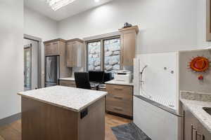 Kitchen with freestanding refrigerator, light wood-style floors, a center island, and light stone counters