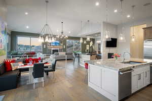 Kitchen featuring open floor plan, stainless steel dishwasher, wood finished floors, vaulted ceiling, and an island with sink