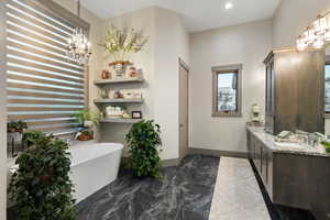 Bathroom featuring marble tiled floors, a freestanding tub, double vanity, a chandelier, and recessed lighting